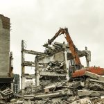 Hydraulic excavator demolition an old building at cloudy sky background Hydraulic excavator demolition an old building at cloudy sky background